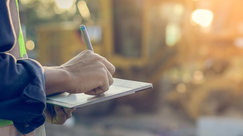 A close up on a hand writing on a clipboard at a health and safety inspection on an agricultural site